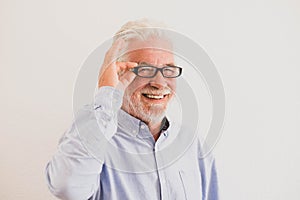 Close up and potrait of mature man smiling and looking at the camera with a white wall at the background - active senior concept