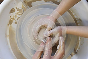 Close-up of a potter`s hands and a child`s hand with an item on a potter`s wheel. Working with clay