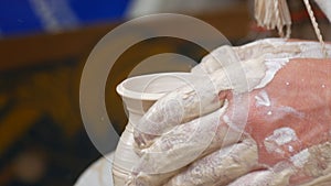 Close-up of potter's hands covered with clay making beautiful vase on throwing wheel in pottery workshop. Creativity