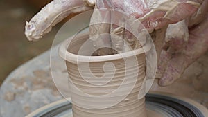 Close-up of potter's hands covered with clay making beautiful vase on throwing wheel in pottery workshop. Creativity