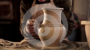 Close up of potter`s hands designing pattern on traditional pottery by chisel with blurry other equipments on desk, clay