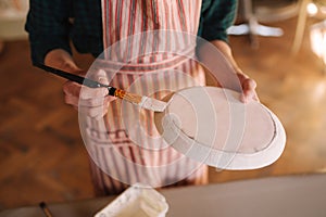 Close up of potter`s hands making ornament on ceramic product. Plate in male`s hands. Young artist