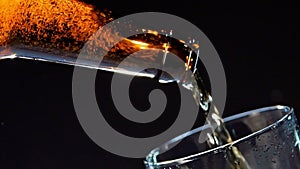 Close up of pouring beer from the glass brown bottle into the glass. Video. Pouring alcoholic drink isolated on black