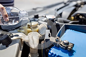 Close up,Pouring clean water from plastic bottle into the windshield washer fluid tank of a car,filling the windshield washer