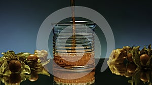 Close up of pouring fruit drink inside an empty glass. Stock clip. Bar counter decorated by small yellow berries on the