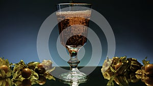 Close up of pouring fruit drink inside an empty glass. Stock clip. Bar counter decorated by small yellow berries on the