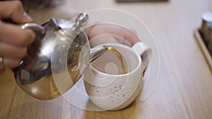 Close-up pouring green herbal tea from teapot in cup. Unrecognizable young Caucasian woman pouring healthful detox