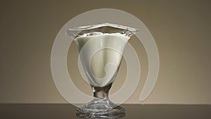 Close up of pouring milk or yogurt into the transparent glass isolated on beige wall background. Stock footage. Concept