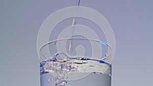 Close up of pouring purified fresh clean drinking water into glass, blue background.