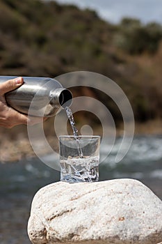Close up pouring purified fresh water from the bottle on glass cup in nature
