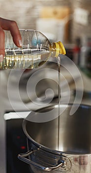 Close up of pouring vegetable oil into deep stainless steel pot