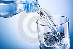 Close-up pouring water from bottle into glass on blue backgrou