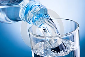 Close-up pouring water from bottle into glass on blue background