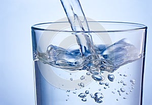 Close-up pouring water into glass on blue background