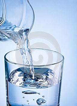 Close-up pouring water from a jug into glass on a blue background