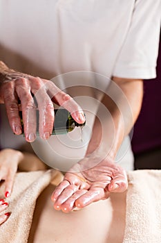 Close-up pours oil in the palm. Osteopath doing manipulative massage on female abdomen. Man hands massaging female