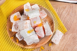 Close-up of a powdered turkish delight. Plate of fruit rahat lokum on a wooden background. Exotic confectionery sweets.