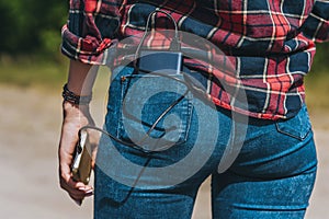 Close-up, Power Bank in the back pocket of the girl`s jeans. Against the backdrop of nature