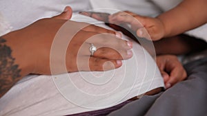 Close-up pregnant belly of African American young woman with hands caressing tummy. Unrecognizable husband wife and