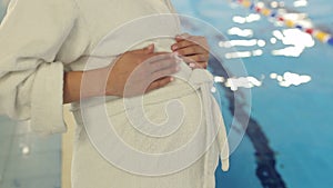 Close-up of a pregnant belly in a Bathrobe by pool