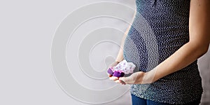 Close up on pregnant belly. Woman expecting a baby with a belly holding baby socks. Copy space