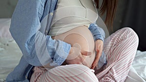 close-up of pregnant belly, woman stroking belly waiting for baby sitting on bed, surrogacy, motherhood and pregnancy