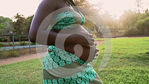 Close up pregnant belly of young African woman in park during sunset time