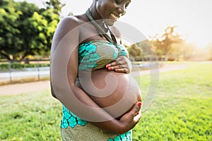 Close up pregnant belly of young African woman in park during sunset time