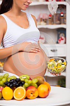 Close-up of a pregnant tummy with fresh fruit and plate of salad. Healthy pregnancy, diet and vitamins