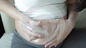 Close up of pregnant woman applying moisturizing cream on her belly  sitting on bed