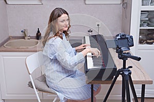 Close-up of a pregnant woman in a blue nightie at a musical instrument, a piano in the home kitchen