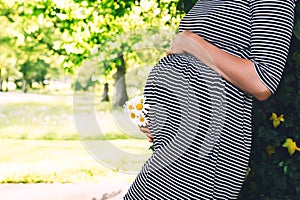 Close-up of pregnant woman with flowers on nature background.