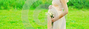 Close up of pregnant woman with flowers in sunny summer day