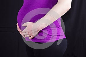 Close-up of pregnant woman with hands over tummy at black backg