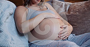 Close up pregnant woman in her active wear on her sofa touching her baby bump