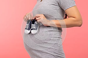 Close up pregnant woman holding baby sneakers for baby newborn isolated on pink background.Pregnant woman packing baby stuff ready