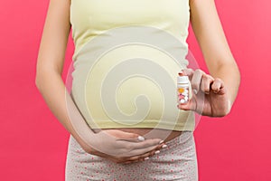 Close up of pregnant woman holding a bottle of pills against her belly at colorful background with copy space. Taking medication