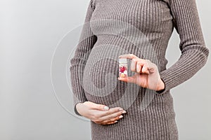 Close up of pregnant woman holding a bottle of pills against her belly at colorful background with copy space. Taking medication