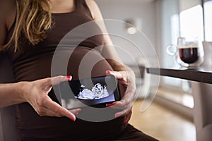 Close Up Of Pregnant Woman Holding Mobile Phone With Ultrasound Scan Of Baby