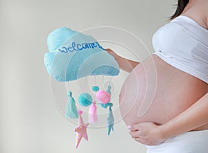 Close-up pregnant woman holding soft fabric mobile with text `Welcome Baby` at tummy