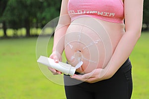 Close-up of pregnant woman mother belly, apply lotion prevent stretch marks over grass lawn meadow sunset outdoor nature summer