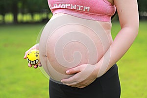 Close-up of pregnant woman mother belly, hold yellow toy smile emoji keep healthy positive attitude