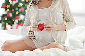 Close up of pregnant woman with red heart in bed