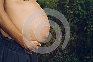 Close-up of pregnant woman`s belly stroking with her hands in nature