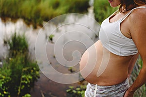 Close-up of pregnant woman`s belly stroking with her hands in nature