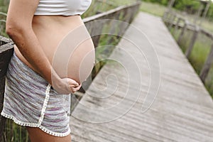 Close-up of pregnant woman`s belly stroking with her hands in nature
