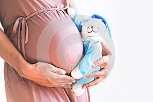Close-up pregnant woman`s belly with teddy toy bear.