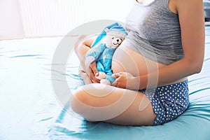 Close-up pregnant woman`s belly with teddy toy bear.