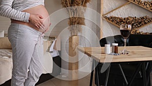 Close-up of a pregnant woman`s stomach, next to a glass of red wine and pills.