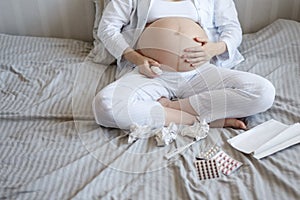 Close-up of a pregnant woman sitting on the bed, cold, with nose spray, pills and thermometer. copy space